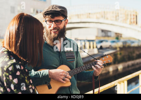 Hipster couple playing ukulele by canal Stock Photo