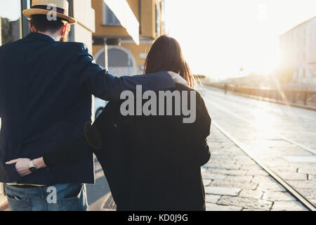 Rear view of couple strolling along sunlit sidewalk Stock Photo