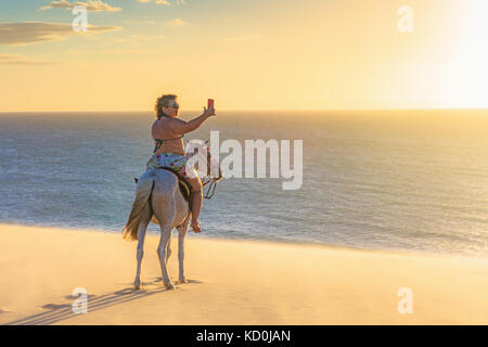 Woman riding horse on beach, taking picture of view using smartphone, Jericoacoara, Ceara, Brazil, South America Stock Photo
