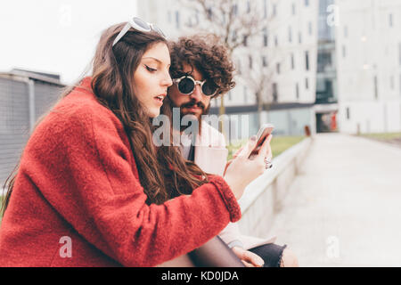 Young couple sitting outdoors, looking at smartphone Stock Photo