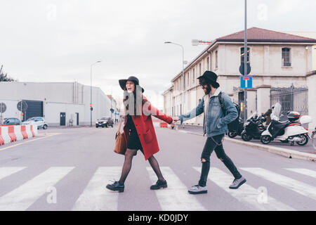 Young couple crossing road, holding hands, laughing Stock Photo