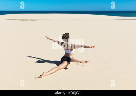 Rear view of woman on beach doing the splits, arms open in yoga position Stock Photo