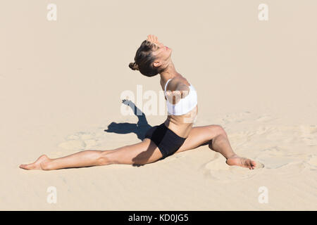 Side view of woman on beach doing the splits, arms open in yoga position Stock Photo