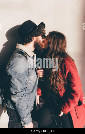 Young couple standing against wall, kissing Stock Photo