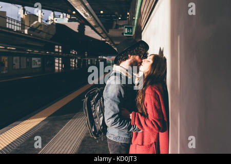 Young couple standing on train platform, kissing Stock Photo
