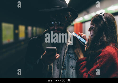 Young couple sitting on subway platform, looking at smartphones Stock Photo