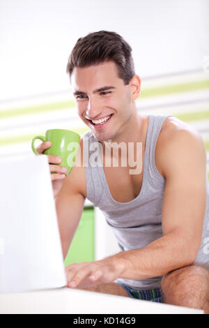 Young smiling men drinking coffee and using laptop in morning Stock Photo