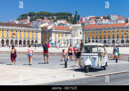 Lisbon, Portugal - August 12, 2017: White Tuk Tuk taxi cab stands on Commerce Square in Lisbon. Ordinary people and tourists walk nearby Stock Photo