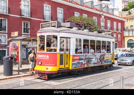 Lisbon, Portugal - August 13, 2017: Red and yellow tram rides down the street, ordinary people and tourists walk nearby