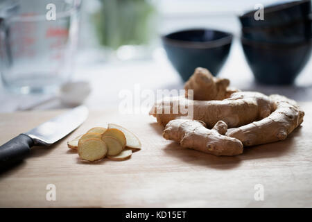 Ginger root and ginger slices with knife on cutting board. Stock Photo