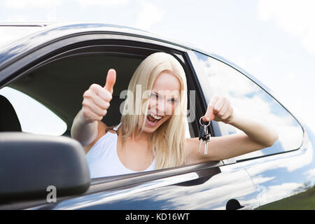 Happy Woman In A Car Showing A Key And Gesturing Thumb Up Stock Photo