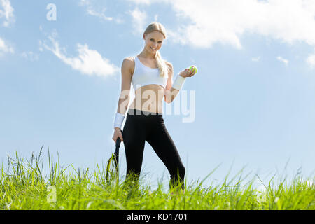 Female Tennis Player Standing In Field Holding Racquet And Ball Stock Photo