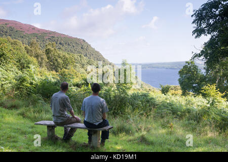 Walkers sitting on a seat in Abriachan Woods Near Drumnadrochit looking at Loch Ness, Scotland. Stock Photo