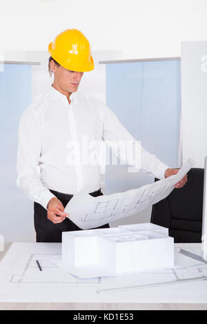 Male Architect Analyzing Blueprint With Architectural Model On Desk Stock Photo