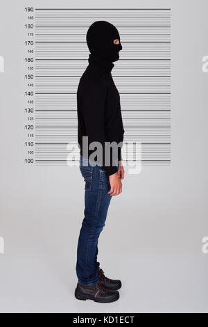 Burglar Wearing Balaclava Standing Against Police Lineup Stock Photo