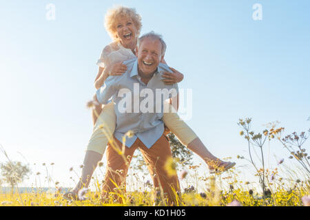 Happy senior man laughing while carrying his partner on his back Stock Photo