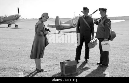 Re-enactment of a lady taking a photograph of two service men with Superrmarine Spitfires in the background at the IWM Duxford Stock Photo