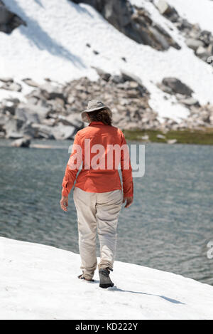 Woman wearing sandles walking on snowfield next to a lake in Oregon's Wallowa Mountains. Stock Photo