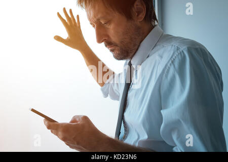 Businessman standing next to office window and using smartphone. Business communication over sms messages or mobile apps. Business person received bad Stock Photo