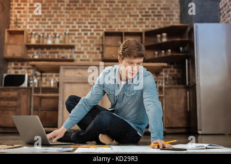 Handsome young man sitting on the floor and working on project Stock Photo