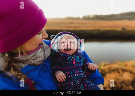 Mid adult woman cradling crying baby daughter on riverbank, Morro Bay, California, USA Stock Photo