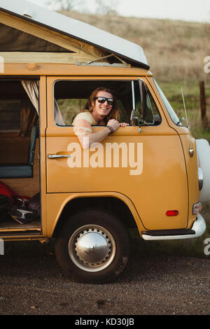 Portrait of long haired young man at vintage recreational vehicle window, Exeter, California, USA Stock Photo