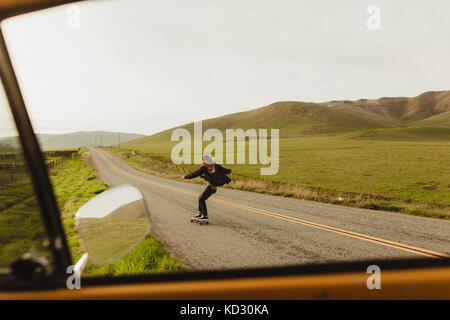 Car window view of young male skateboarder skateboarding along rural road, Exeter, California, USA Stock Photo