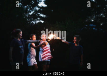 Boy and three girls igniting sparklers together at night on independence day, USA Stock Photo