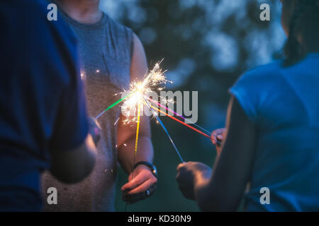 Cropped shot of women and girl igniting sparklers together at dusk on independence day, USA Stock Photo