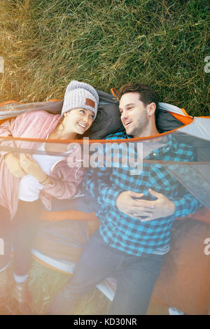 Couple lying in tent, heads outside of tent, smiling, overhead view Stock Photo