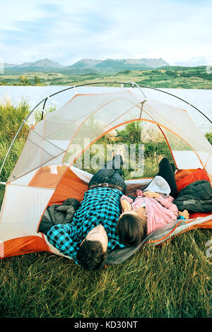 Couple lying in tent, heads outside of tent, rear view, Heeney, Colorado, United States Stock Photo