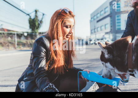 Red haired woman giving dog drink of water Stock Photo