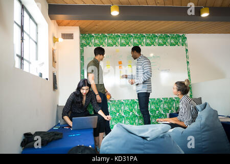 Young businessmen and women using laptop and whiteboard in creative meeting room Stock Photo
