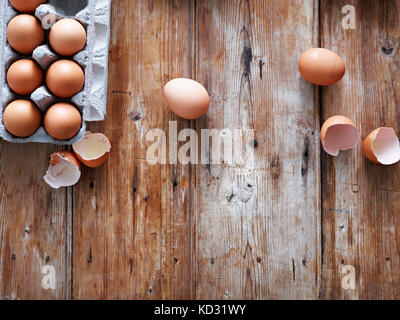 Eggs in egg box and broken shells on wooden surface, overhead view Stock Photo