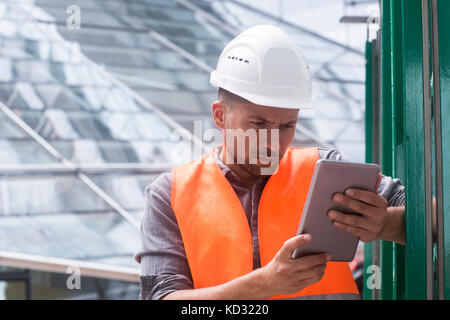 Man wearing hard hat and high viz using digital tablet Stock Photo