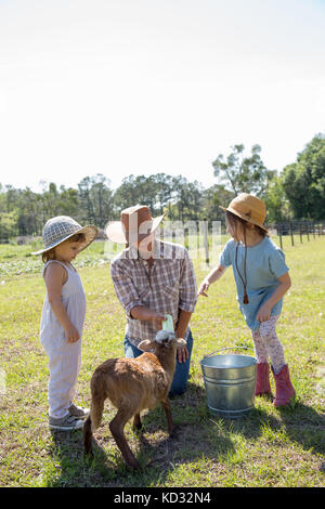 Mother and two children on farm, bottle feeding young goat Stock Photo