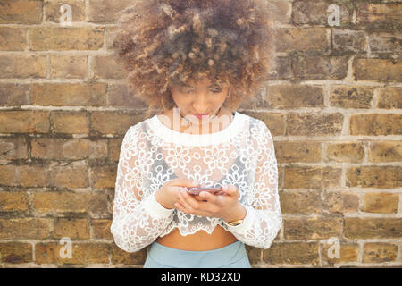 Young woman leaning against wall, using smartphone Stock Photo