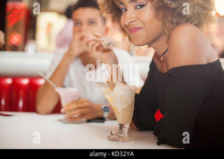 Young couple sitting in diner, eating dessert, smiling