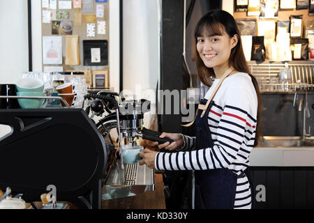 Portrait of smiling asian barista preparing cappuccino with coffee machine. Cafe restaurant service, Small business owner, food and drink industry con Stock Photo