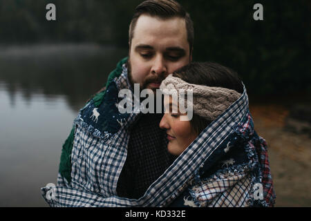 Couple wrapped in blanket eyes closed hugging Stock Photo