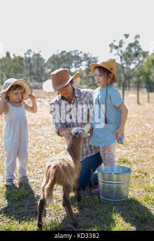 Mother and two children on farm, bottle feeding young goat Stock Photo