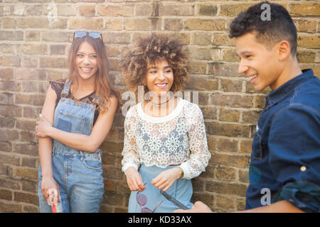 Three friends standing together in street, laughing Stock Photo