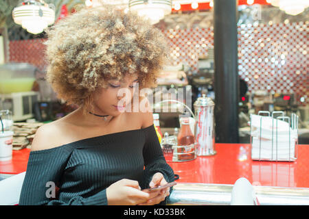 Young woman sitting in diner, looking at smartphone Stock Photo