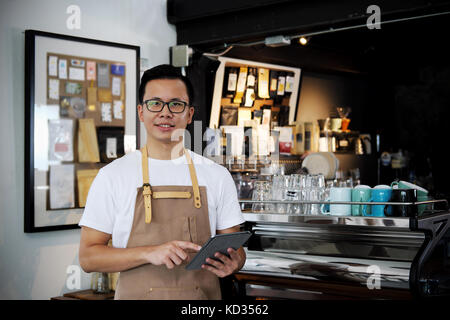 Portrait of smiling asian barista holding digital tablet at counter in coffee shop. Cafe restaurant service, Small business owner, food and drink indu