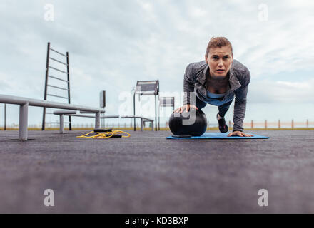 Young and fit sportswoman doing pushups in outdoor gym. fitness woman doing push-ups with exercise ball. Stock Photo