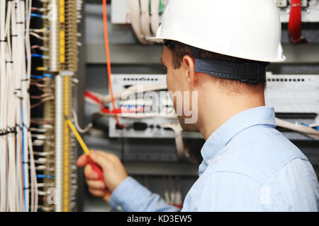 Engineer with screwdriver checking wire connections. Young electrician at work. Stock Photo