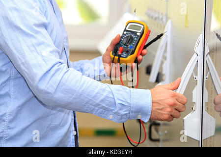 Engineer with multimeter checking voltage supply. Electrician open door to control panel at power station. Stock Photo