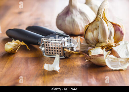Fresh garlic and garlic presser on wooden table. Stock Photo