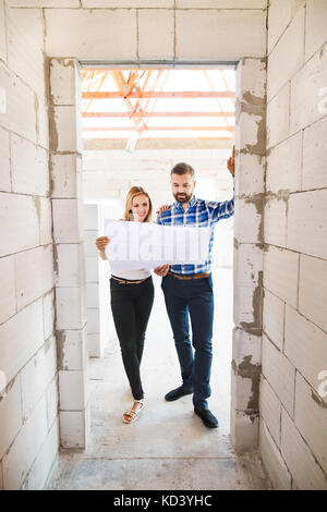 Young couple or architects or civil engineers looking at plans of the new house, discussing issues at the construction site. Stock Photo