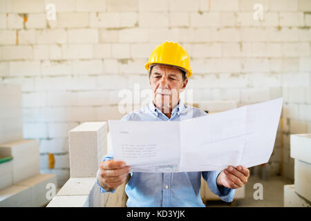 Senior architect or civil engineer at the construction site with blueprints, controlling issues at the construction site. Stock Photo